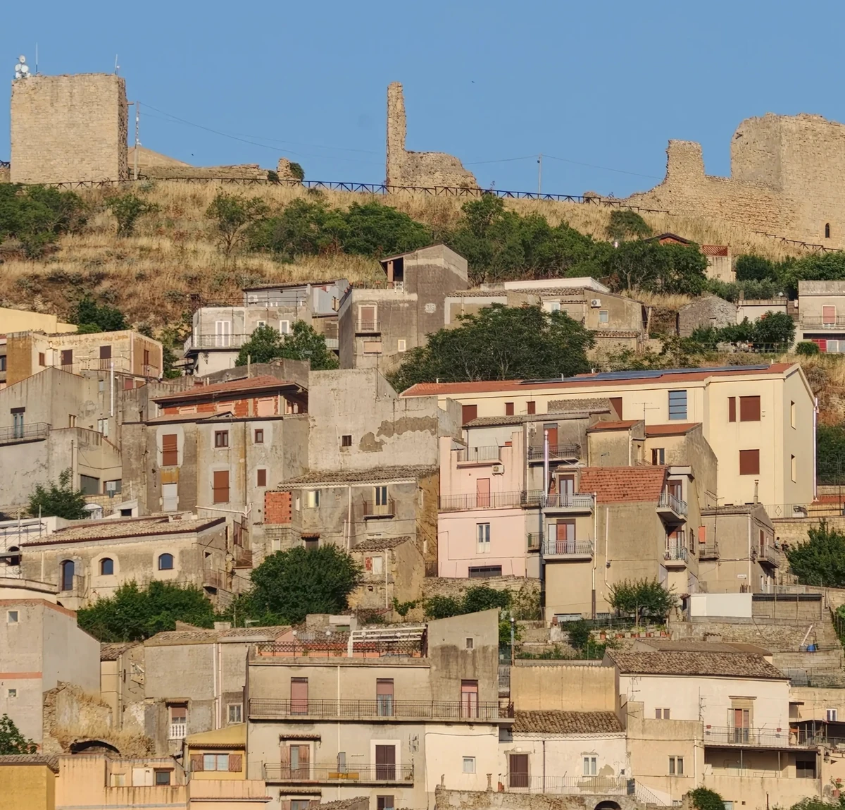 Le torri e le mura del castello di Agira, sopra le case del paese, sotto un cielo azzurro.