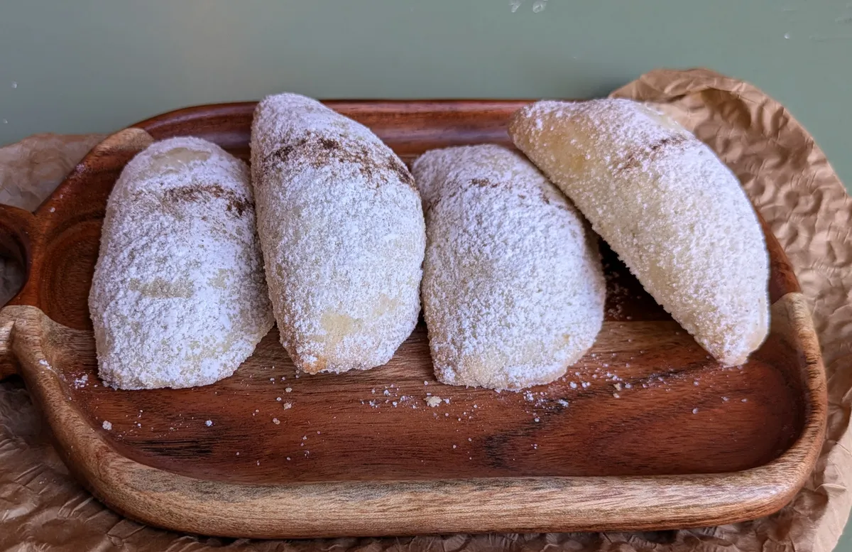Four sugar-dusted cassatelle di Agira on a wooden serving plate.
